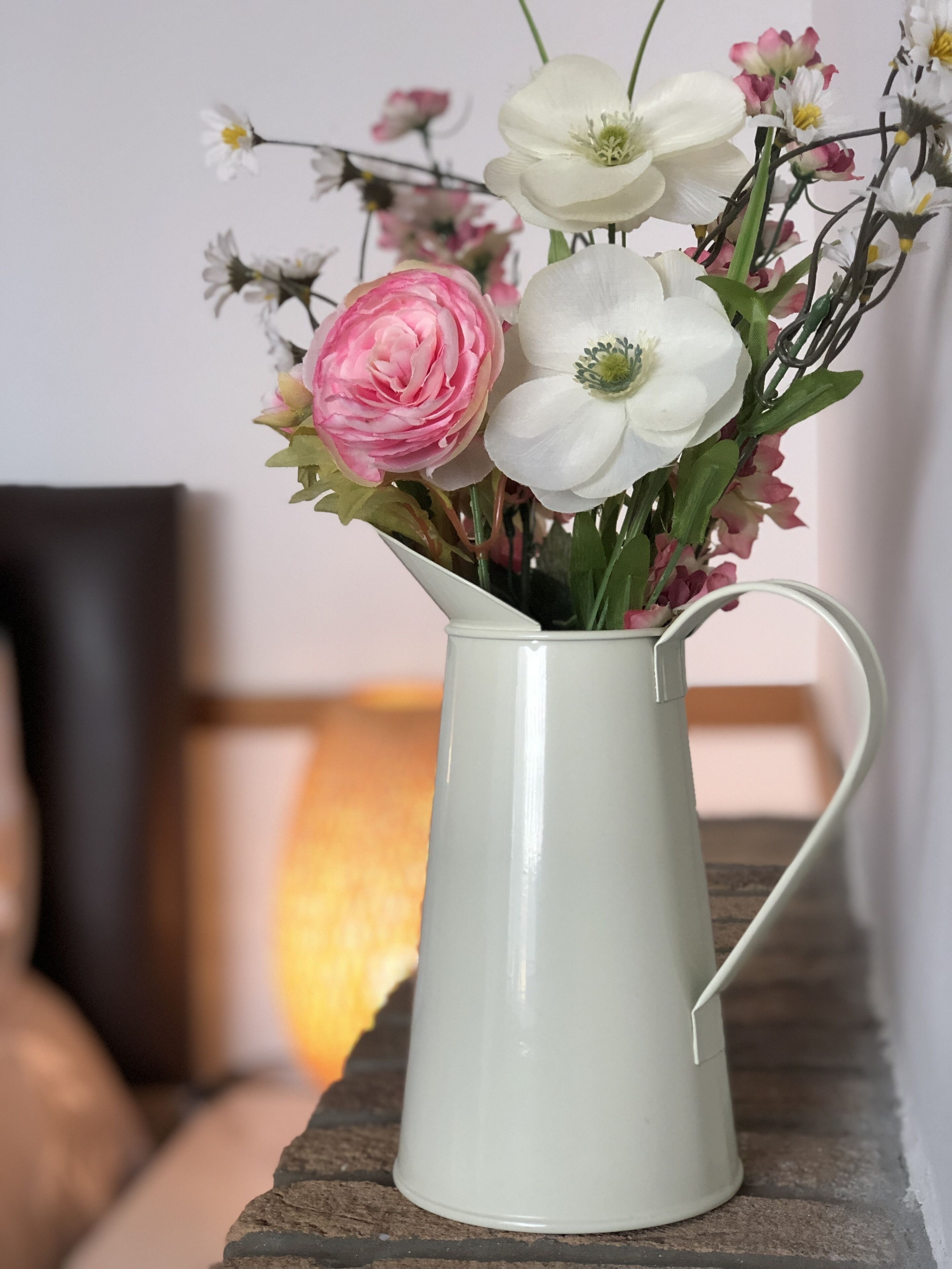 Un boccale di ceramica bianca colmo di fiori, posato su un piano di legno.