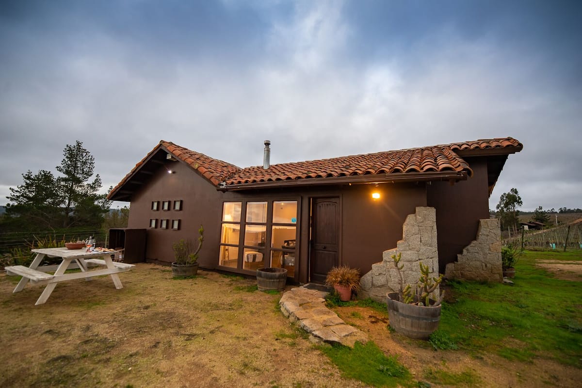 Una casa rústica con fachada marrón, ventanas grandes y techo de tejas.