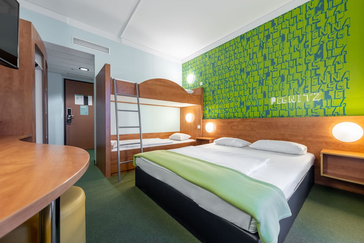 A hotel room with a bunk bed, a desk, and a green patterned wall.