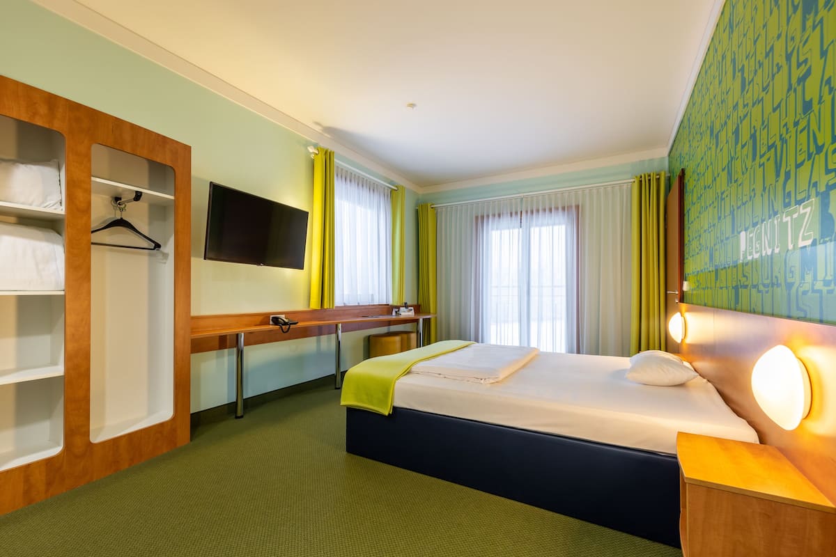 A hotel room with a bed, a desk, a TV, and a wardrobe.