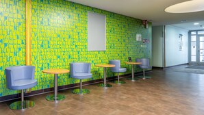 Un hall con una pared de patrón vibrante en amarillo y azul, una pizarra y varias sillas y mesas redondas azules.