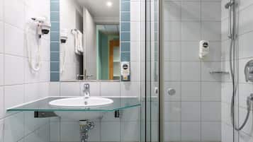 Une salle de bain moderne avec un lavabo en verre, une douchette à main et un sèche-cheveux fixé au mur.
