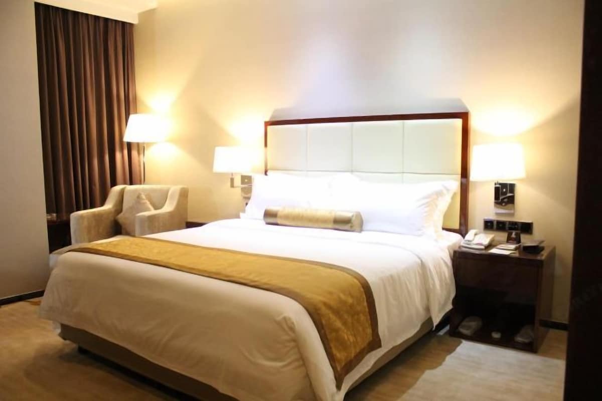 A hotel room with a large bed, two bedside lamps, a chair, and a nightstand with a phone.