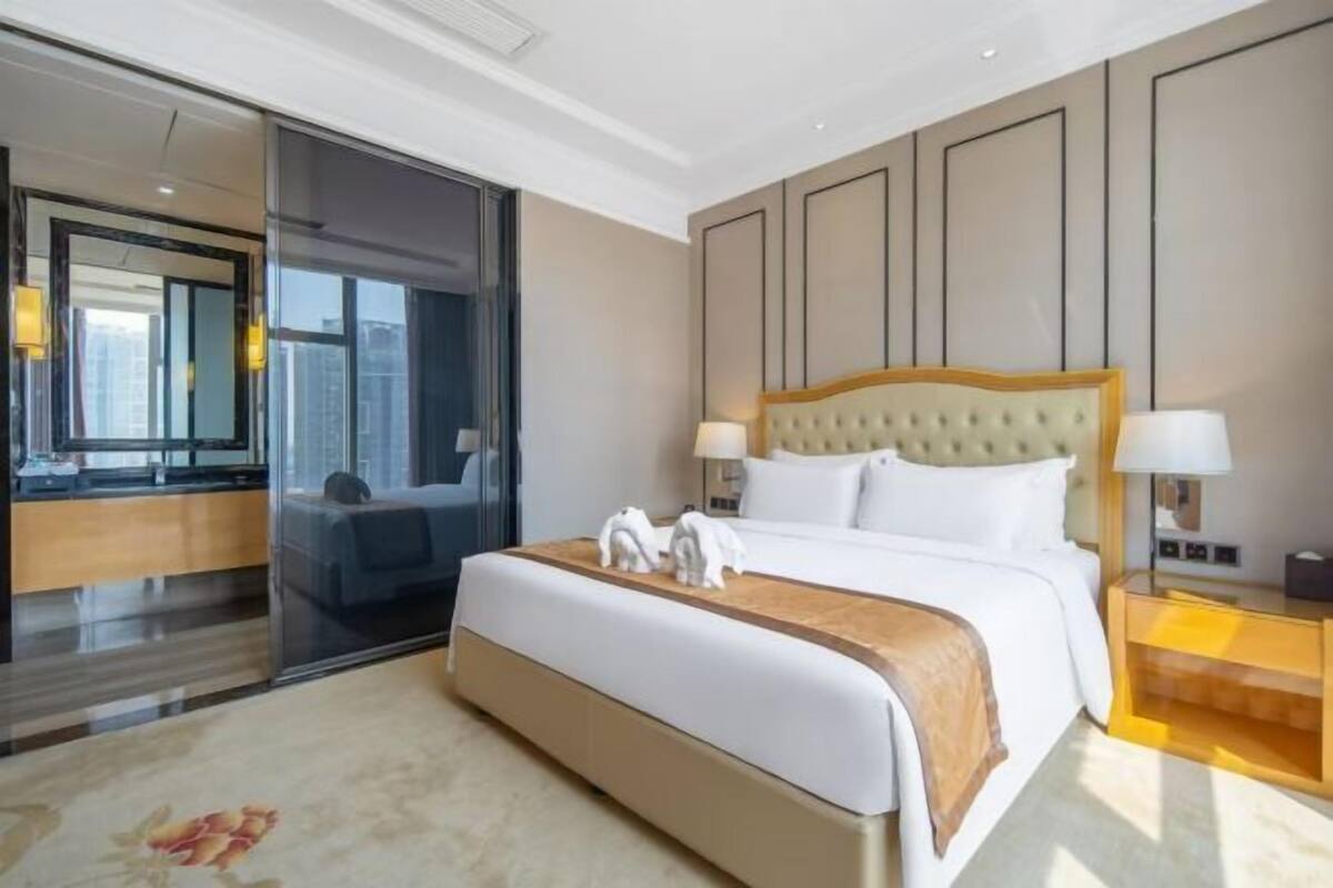 Ein Hotelzimmer mit einem großen Bett, einem Nachttisch mit Lampen, einem Spiegel und Blick auf die Stadt.