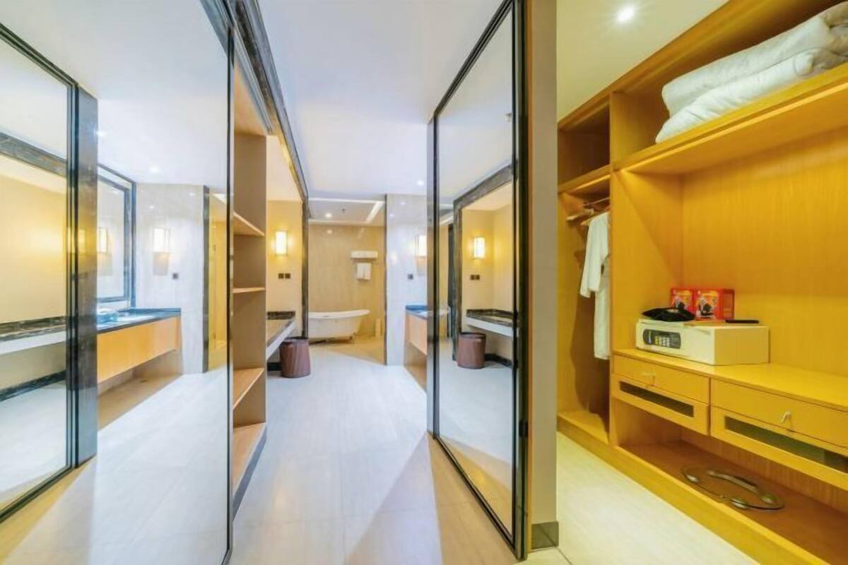 Ein modernes Hotelzimmer mit einem gläsernen Badezimmer, einem Holzanrichte und einem ordentlich eingerichteten Kleiderschrank.