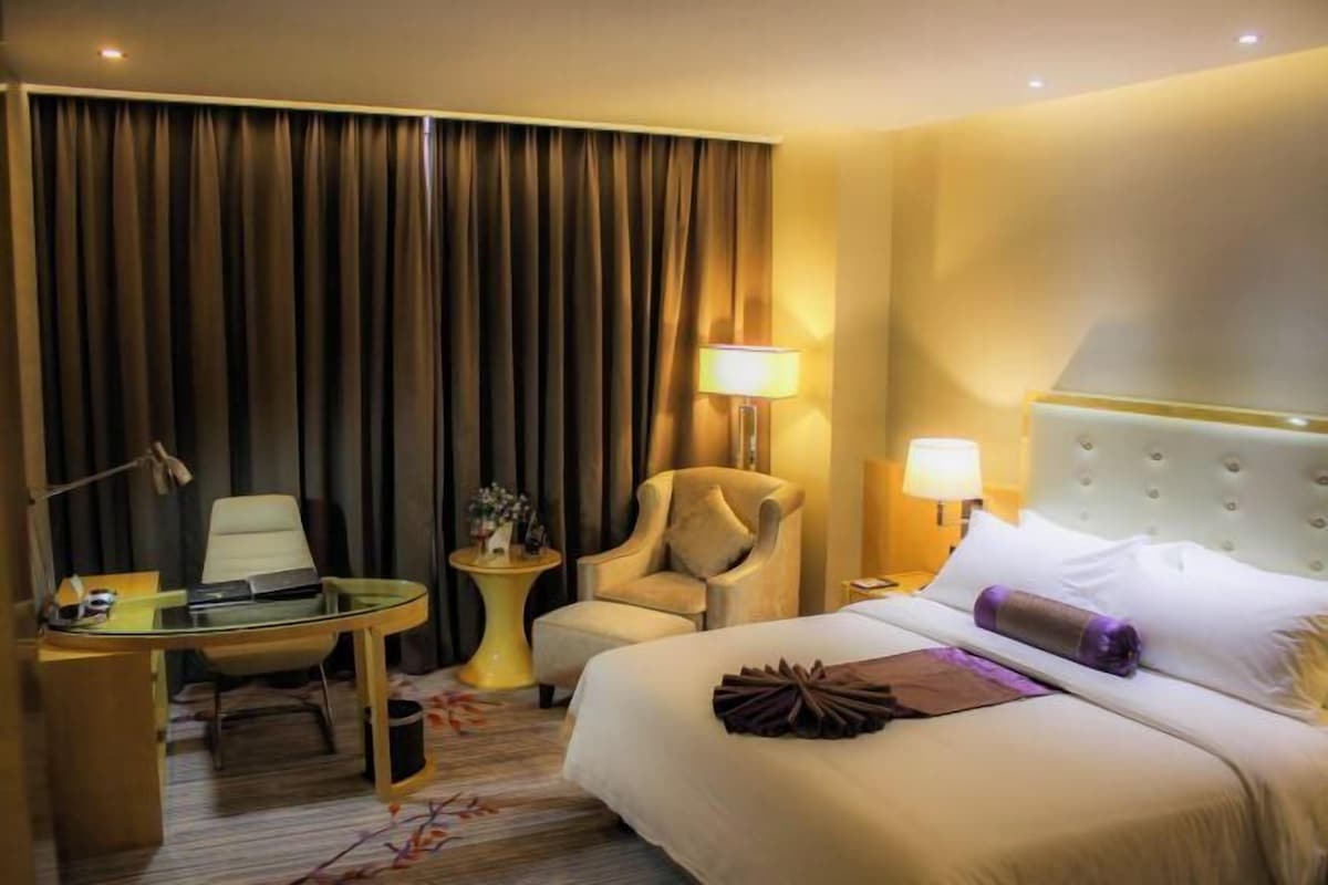 A hotel room with a bed, a desk, a chair, a lamp, and a curtain.