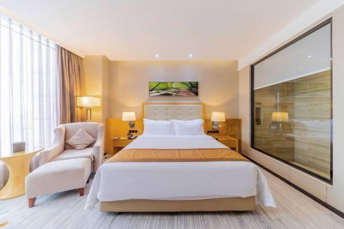 Ein Hotelzimmer mit einem großen Bett, einem Sessel, einem Nachttisch und einem großen Fenster.