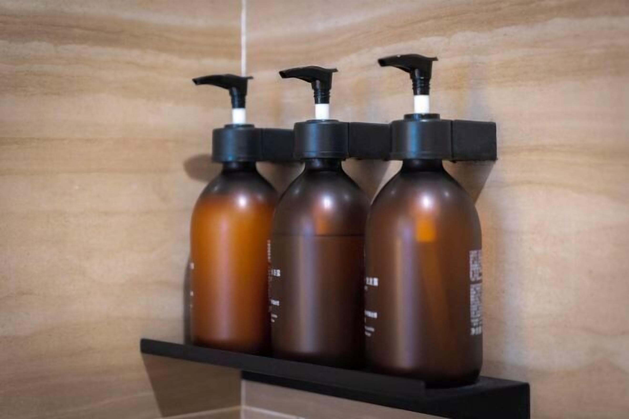 Three brown bottles with black pumps on a black shelf against a beige wall.