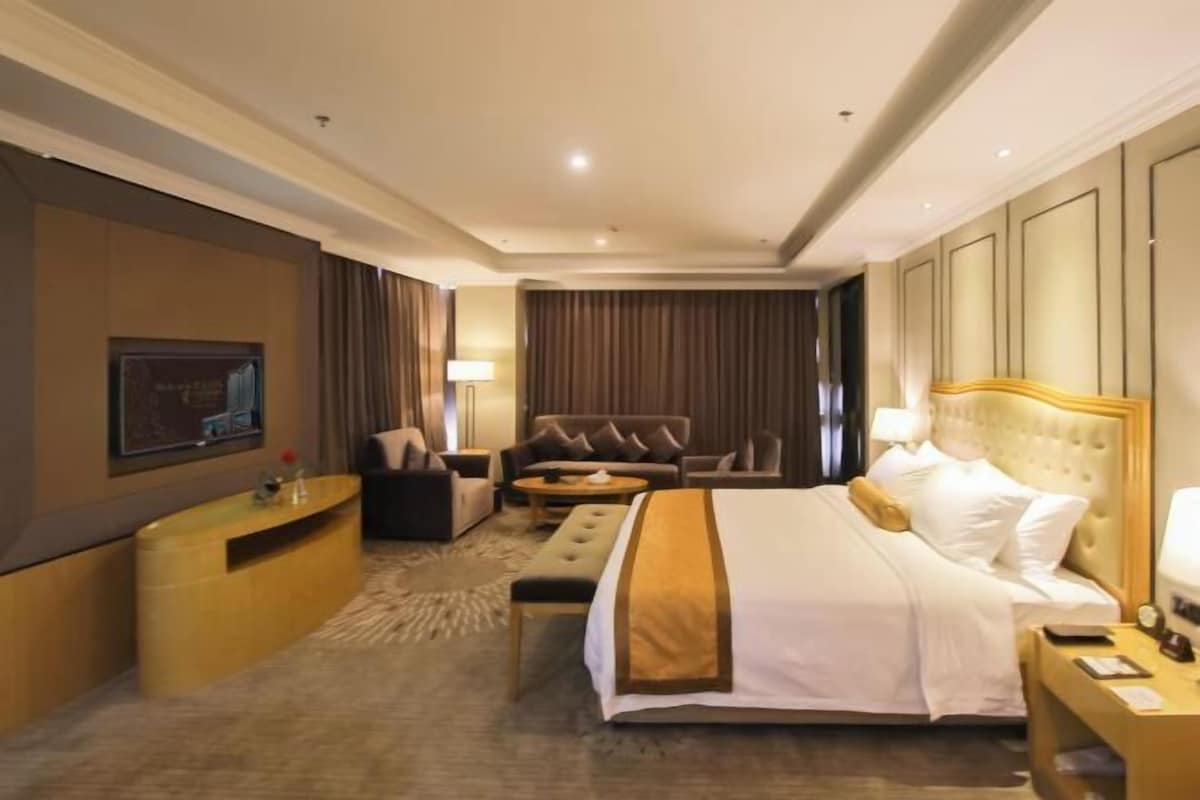 A hotel room with a large bed, a sofa, a desk, and a television.
