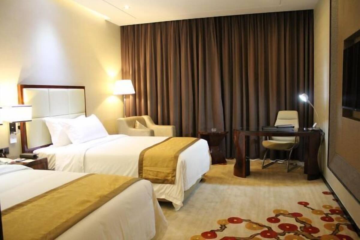 Ein Hotelzimmer mit zwei Betten, einem Schreibtisch, einem Stuhl und einem großen Fenster mit Vorhängen.