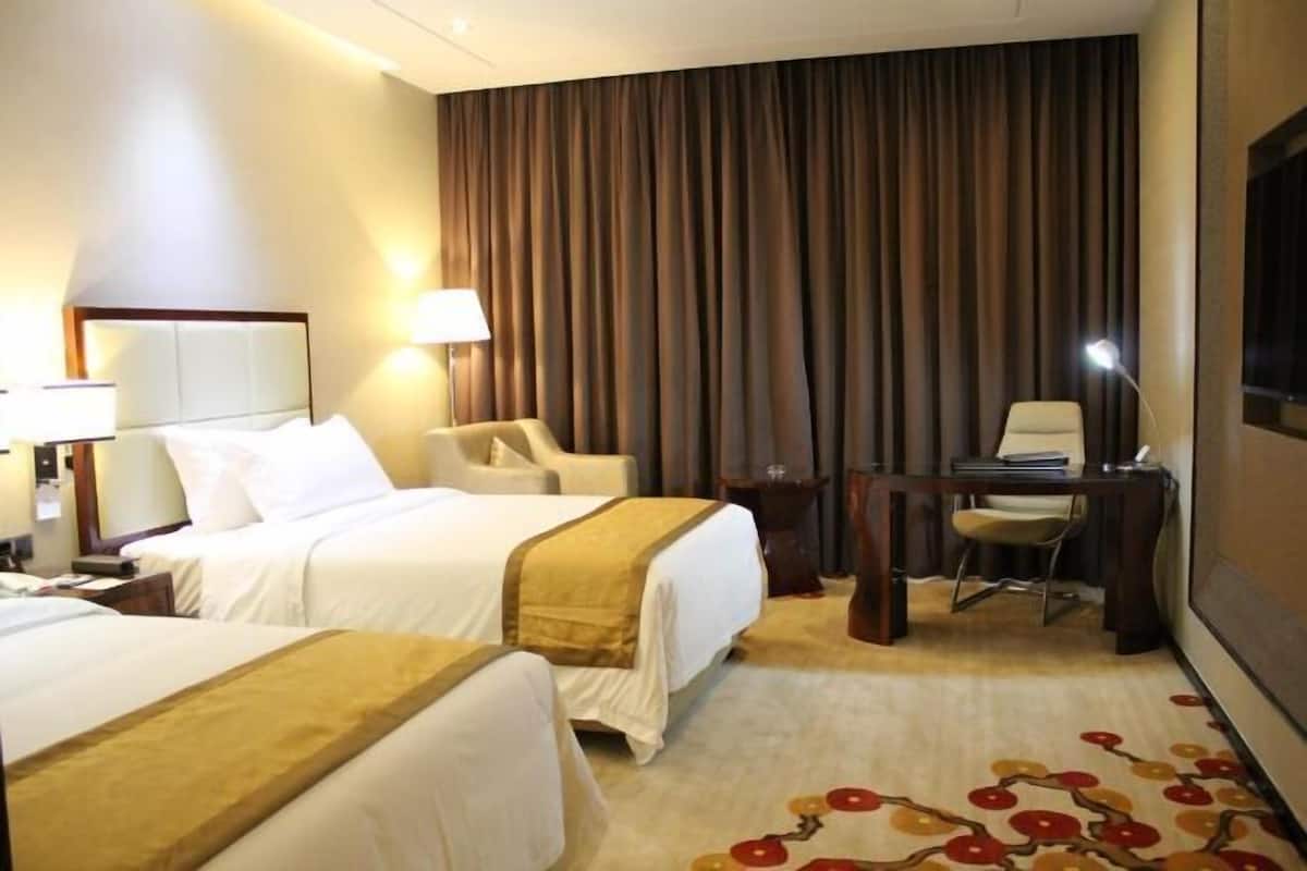 Une chambre d’hôtel avec deux lits, un bureau, une chaise et une grande fenêtre avec des rideaux.