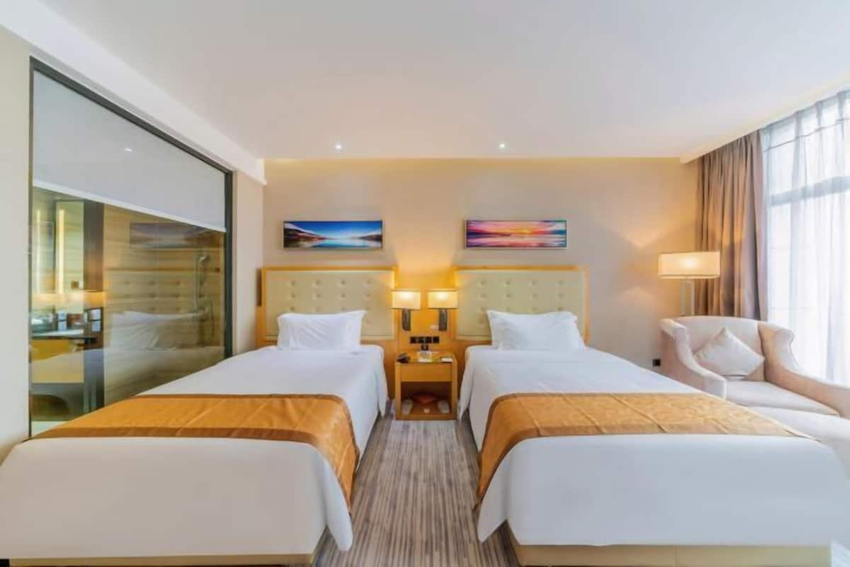 Une chambre d’hôtel avec deux lits, un mur en verre, une table de chevet avec des lampes et une chaise.