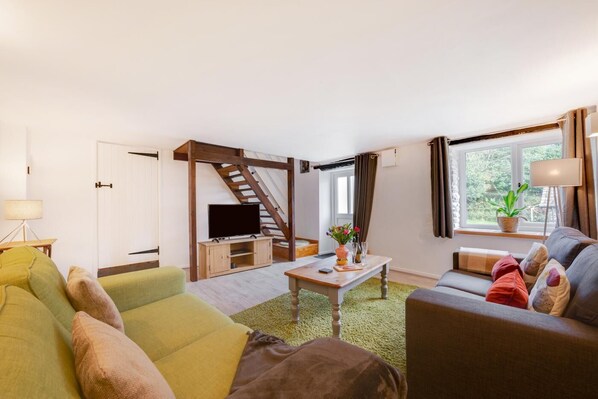 A modern living room with a staircase, a flat-screen TV, a coffee table, and two sofas.