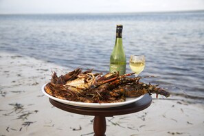 A plate of seafood and a bottle of white wine on a table by the sea. - Kena Beach Villas (Marumbi)