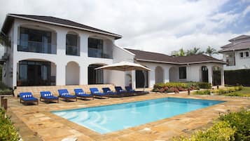Relax by the pool in a spacious outdoor area with lounge chairs and a shaded umbrella, surrounded by well-maintained gardens.