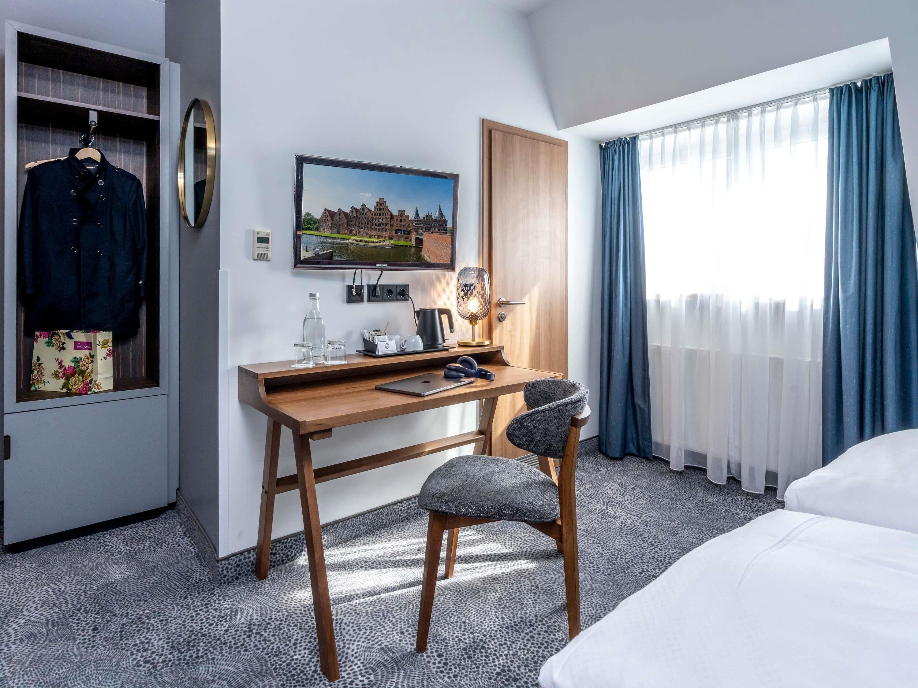 Ein Hotelzimmer mit einem Bett, einem Schreibtisch mit Stuhl, einem Fernseher, einem Kleiderschrank und einem Fenster mit Vorhängen.