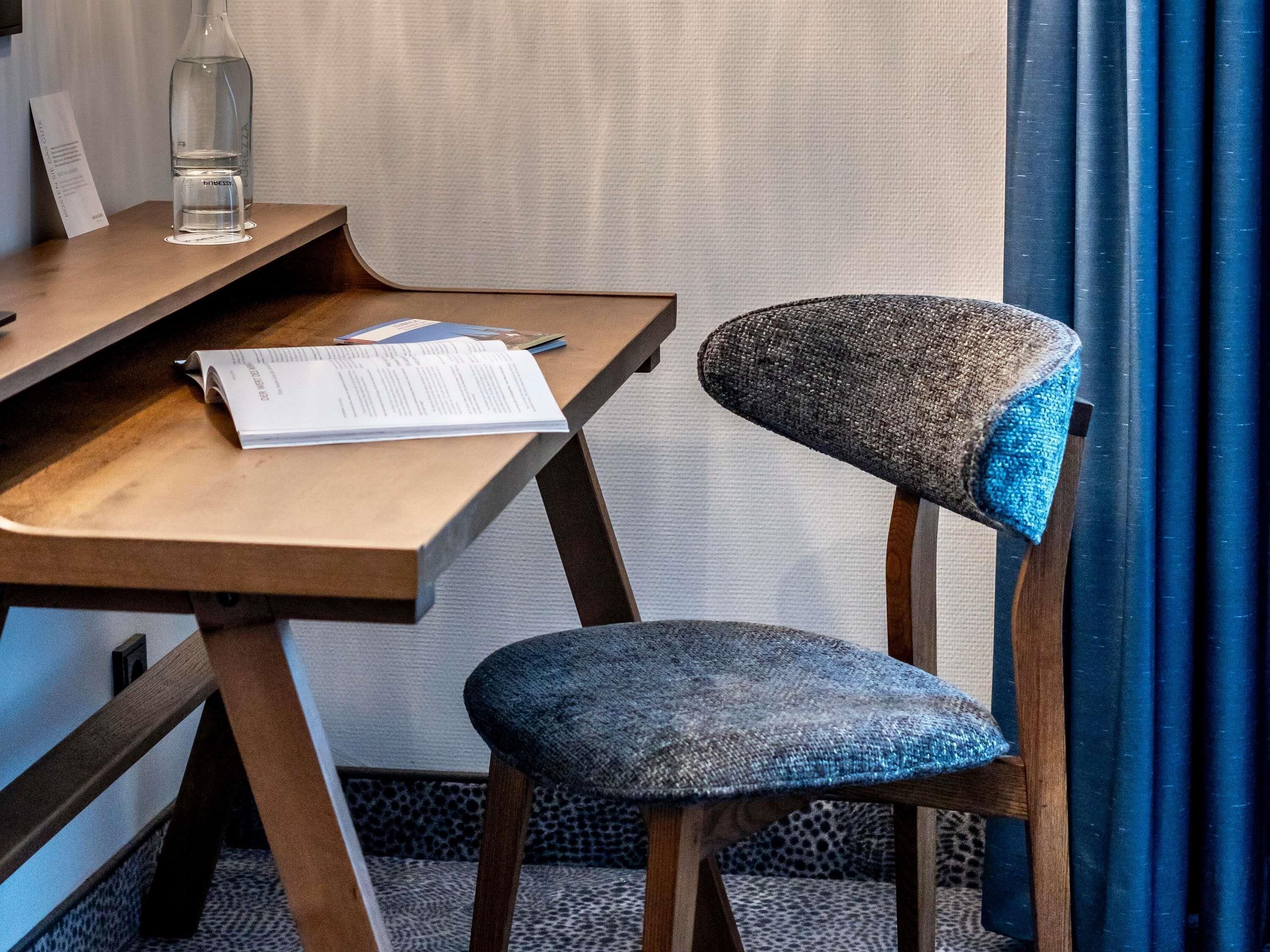 A wooden desk with a chair, a bottle of water, and a menu on the table.