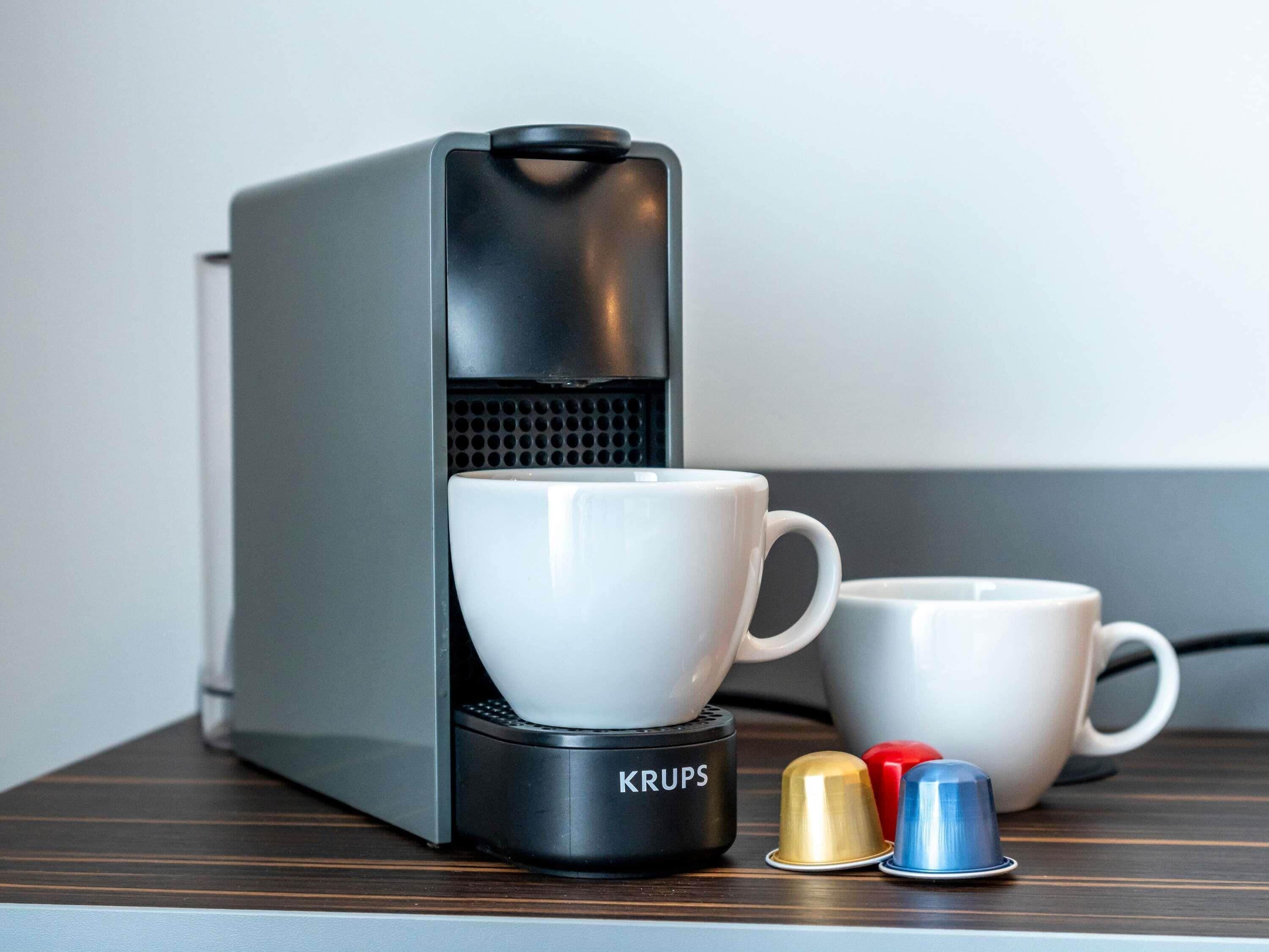Een koffieapparaat met twee witte bekers en drie capsules op een houten oppervlak.