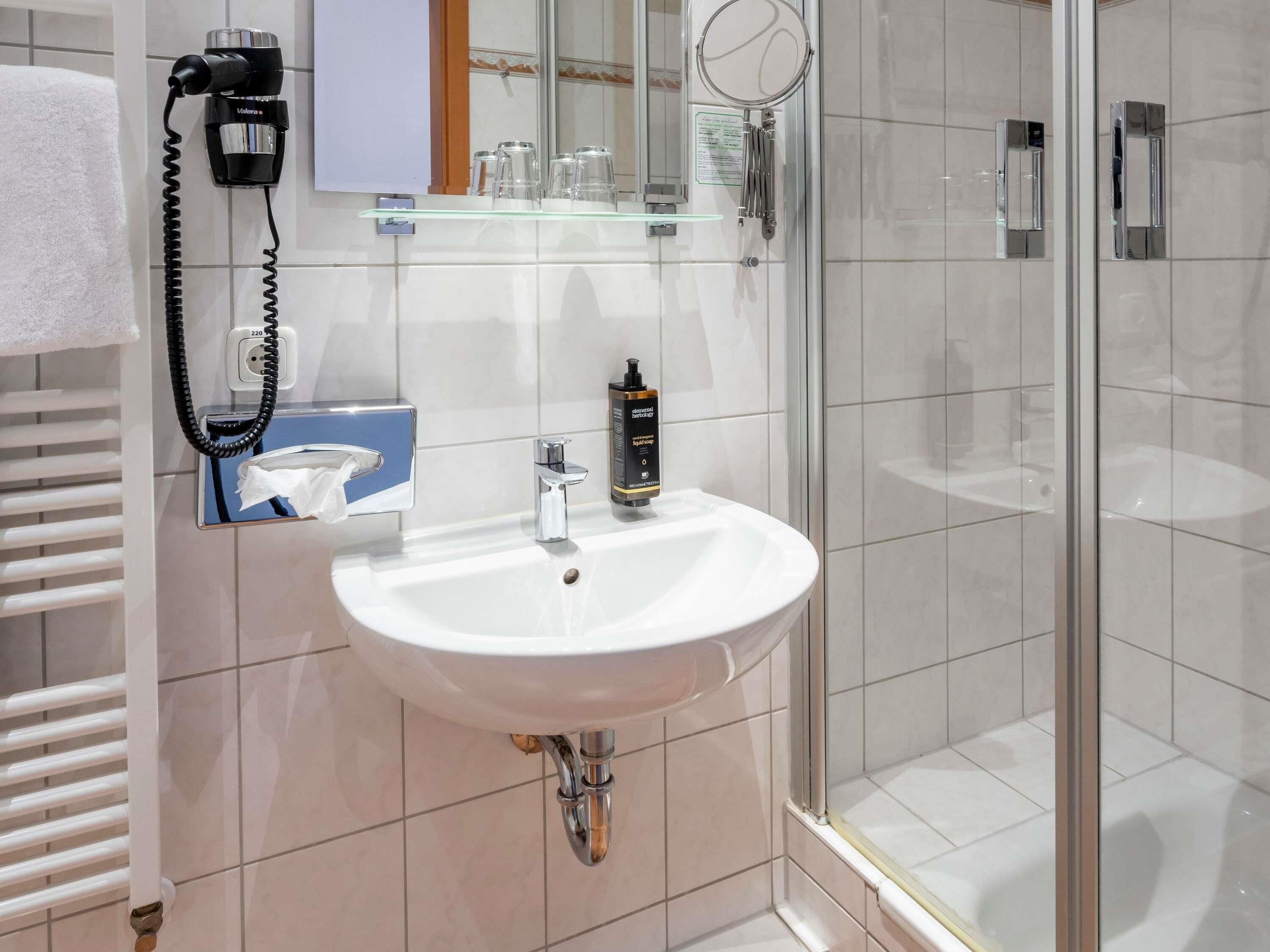 Une salle de bain avec un lavabo blanc, un miroir, une douche en verre et un porte-serviettes.