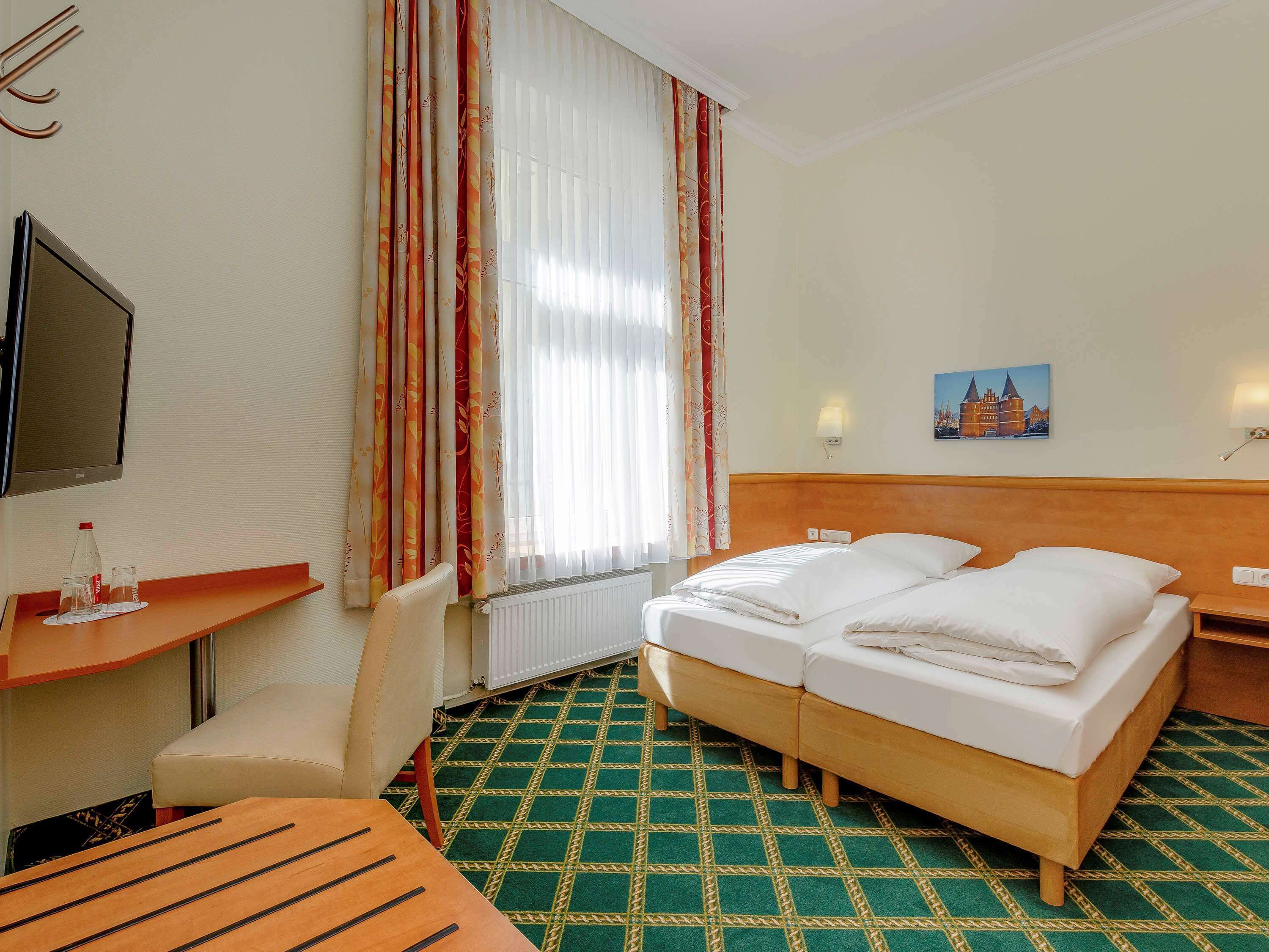A hotel room with a bed, a desk with a chair, a television, and a painting on the wall.