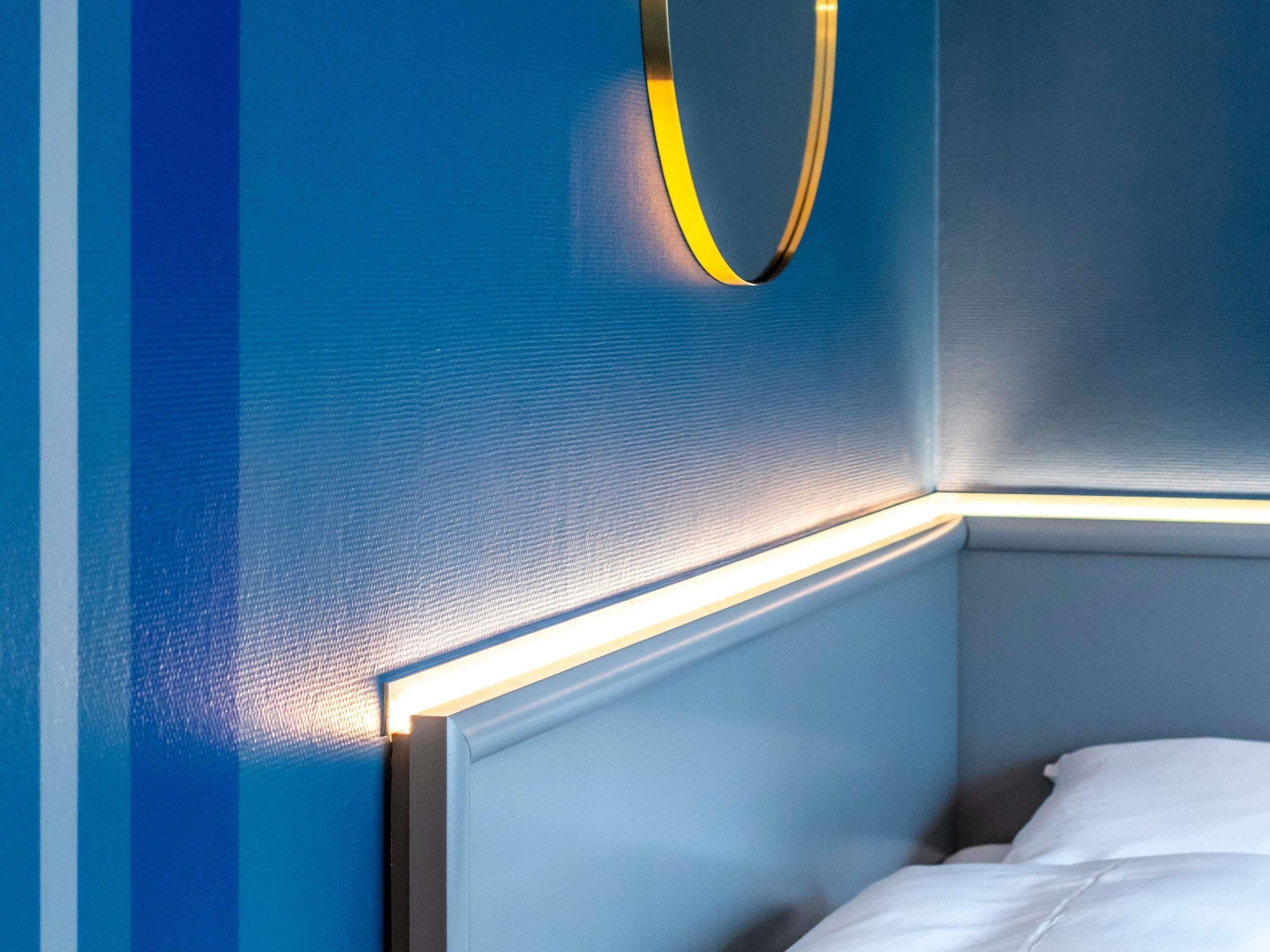 A corner of a room with a bed, a wall with a textured finish, and a light fixture.