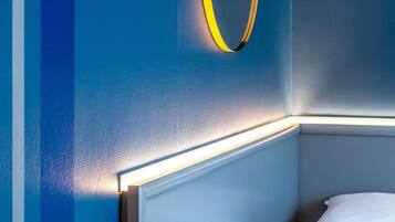 A corner of a room with a bed, a wall with a textured finish, and a light fixture.