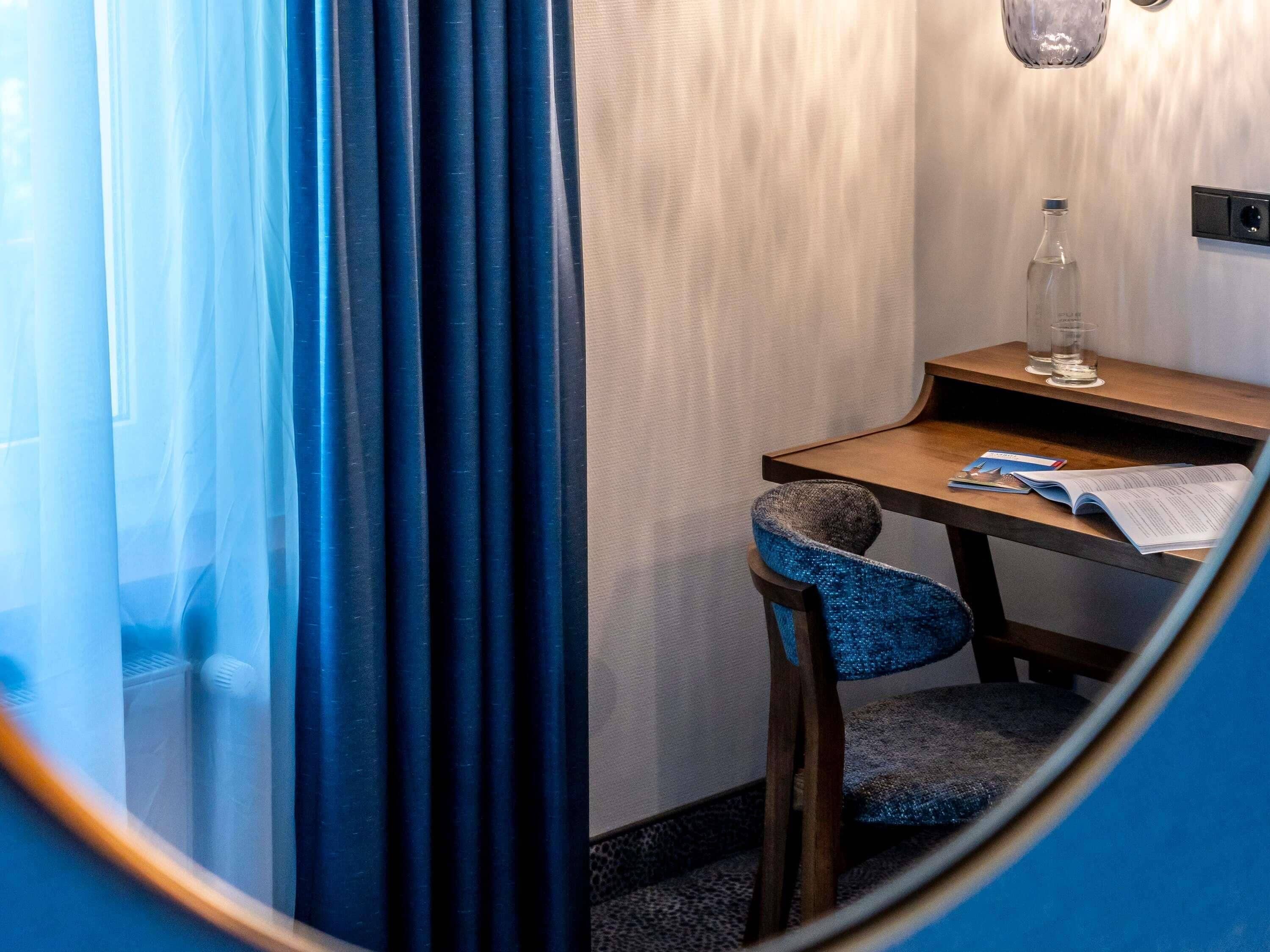 Une petite pièce privée, avec un bureau en bois, une chaise, une bouteille et un verre d’eau posés sur une table de chevet.