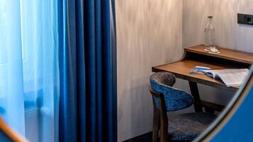 Une petite pièce privée, avec un bureau en bois, une chaise, une bouteille et un verre d’eau posés sur une table de chevet.