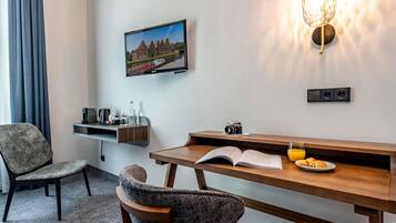Ein Hotelzimmer mit einem Holztisch, einem Stuhl, einem an der Wand befestigten Fernseher, einer Wandleuchte und einem gerahmten Bild.