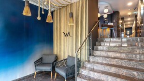 Un vestíbulo moderno con una pared azul, una escalera de peldaños de mármol y una zona de estar con sillas.