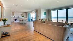 A spacious living area with a large window overlooking a beach, a kitchen with modern appliances, and a dining area with a table and chairs. - 2 Bed in Westward Ho! (oc-seaspr) (Westward Ho!)
