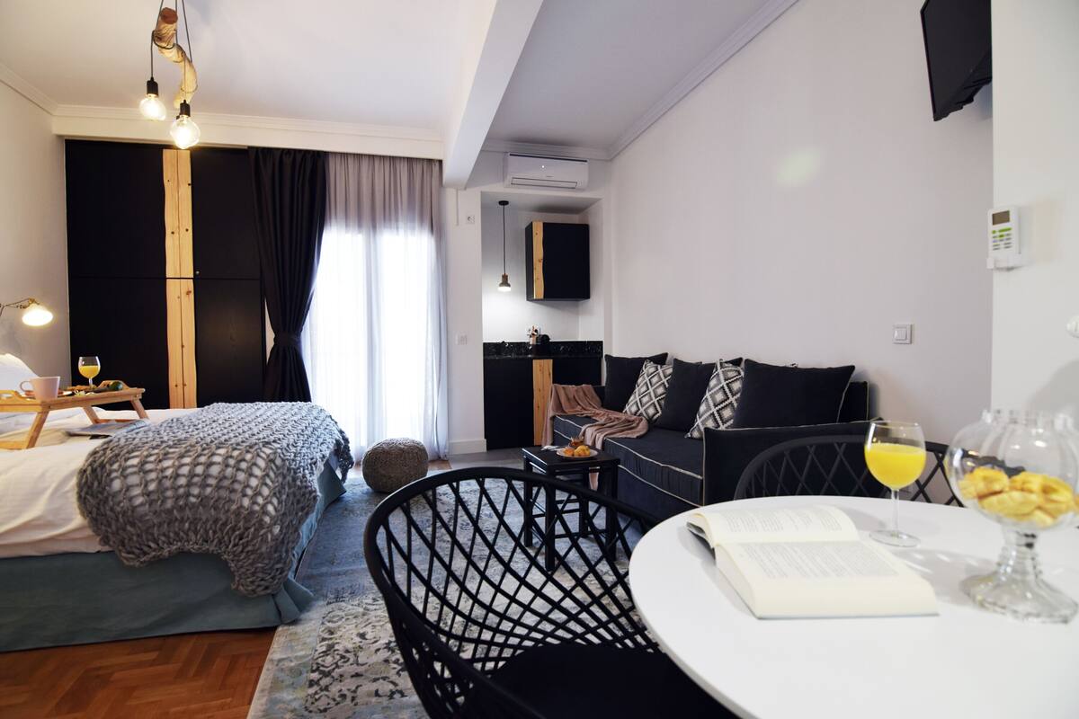 Ein modernes Hotelzimmer mit Bett, einer Couch, einem Esstisch und einer kleinen Küchenzeile.