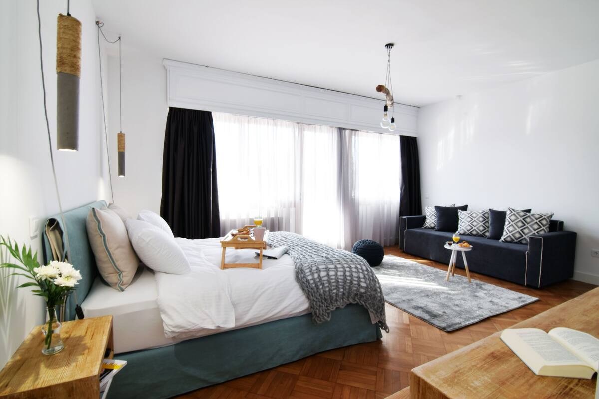 Ein modernes Schlafzimmer mit Bett, Nachttisch und einer Leseecke mit Sessel und Tisch.