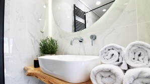 A bathroom with a white sink, a wooden shelf, and a mirror reflecting a towel rack. - Grey Studios (Thessaloniki)