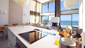 Een moderne keuken met een groot eiland, een eethoek en uitzicht op zee.