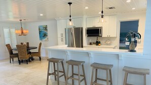 A modern kitchen with white cabinetry, stainless steel appliances, and a bar area with stools. - BEACHY BUNGALOW. Within two miles of beaches/boat ramps. Book your WINTER stay! (Jupiter)