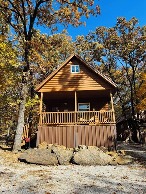 A wooden cabin with a balcony, surrounded by trees and rocks. - Grandma's cabin nestled in a little woodland village – playground, pond and more (Winslow)