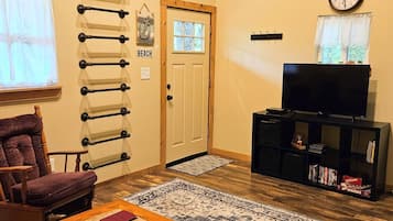 A living room with a wooden coffee table, a television on a stand, a patterned rug, a chair, and a wall-mounted rack.