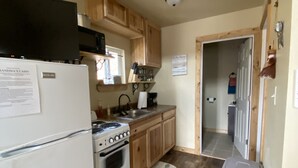 A compact kitchen with wooden cabinets, a white refrigerator, a stove, and a sink. - Grandma's cabin nestled in a little woodland village – playground, pond and more (Winslow)