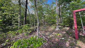 A forested area with a red wooden swing set. - Grandma's cabin nestled in a little woodland village – playground, pond and more (Winslow)