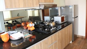 A modern kitchen with wooden cabinets, a black countertop, stainless steel appliances, and various kitchen utensils. - Residencial Cafferata (Lima)