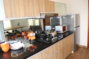 Cozinha moderna com armários de madeira, bancada preta, eletrodomésticos de aço inoxidável e diversos utensílios de cozinha.