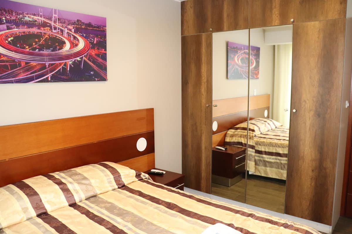 A bedroom with a wooden headboard, a bed with striped bedding, a nightstand, a bedside table, and a large mirror.