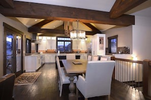 A modern kitchen with white cabinetry, a wooden dining table, and a chandelier.