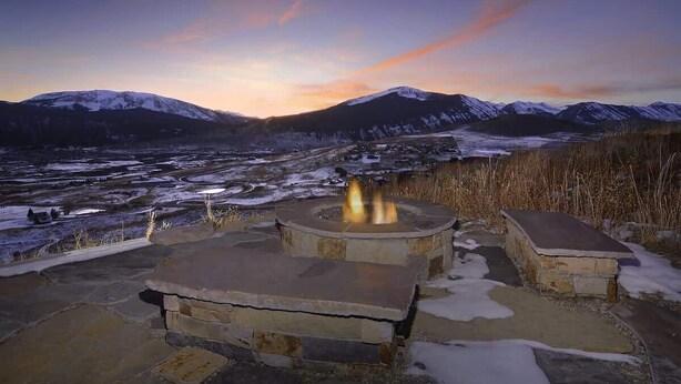 Un espace aménagé avec un foyer en pierre, offrant une vue sur les montagnes enneigées au crépuscule.
