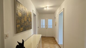 Un pasillo con suelo tipo espiga, paredes blancas y una escultura de conejo negro sobre una mesa blanca.