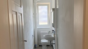 Un baño estrecho con paredes blancas, inodoro, lavamanos y ventana.