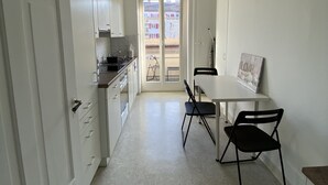 Un pasillo estrecho que lleva a una puerta con vistas a edificios. Hay una mesa pequeña con sillas y un cuadro en la pared.