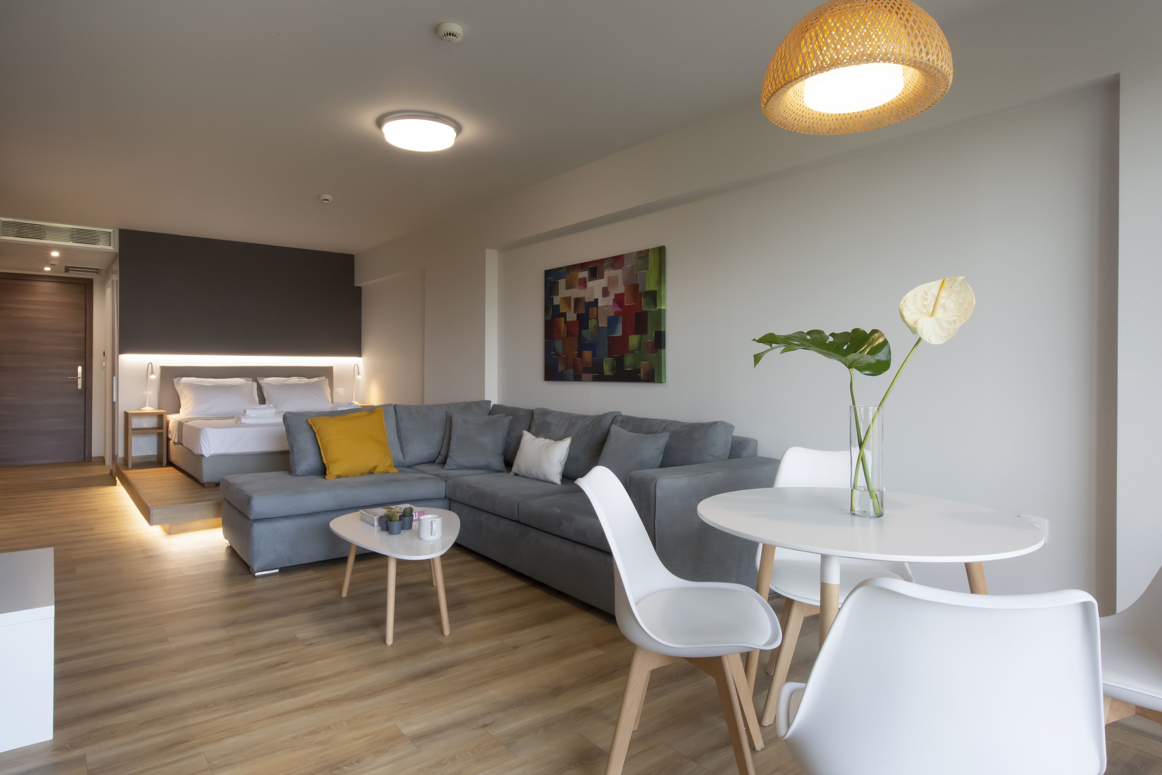 A modern living room with a grey sofa, a white dining table, and a small white side table.