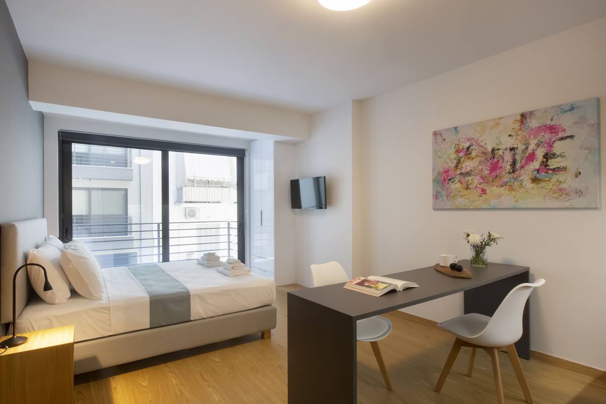 Une chambre moderne avec un lit, une table de chevet et une fenêtre donnant sur un immeuble.